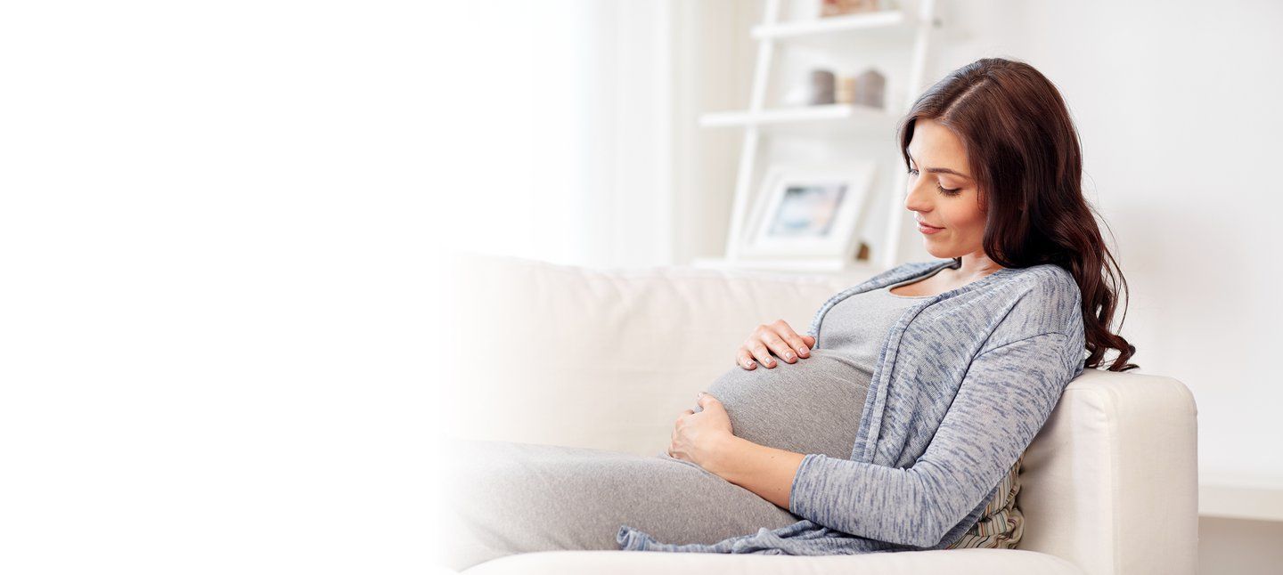 Woman during early pregnancy lying on sofa holding her baby bump