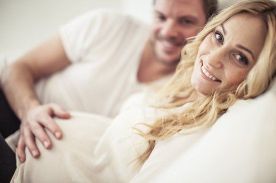 Pregnant women looking into the camera with man's hand on her bump