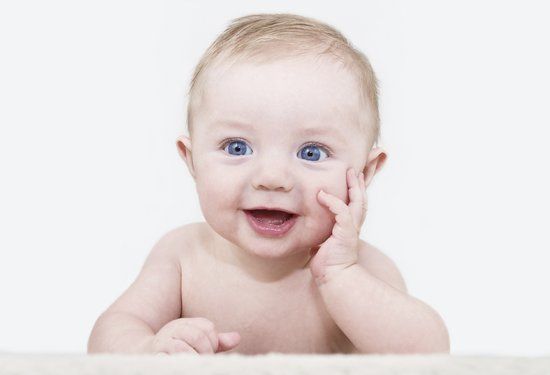 Baby with big blue eyes leaning on his hand