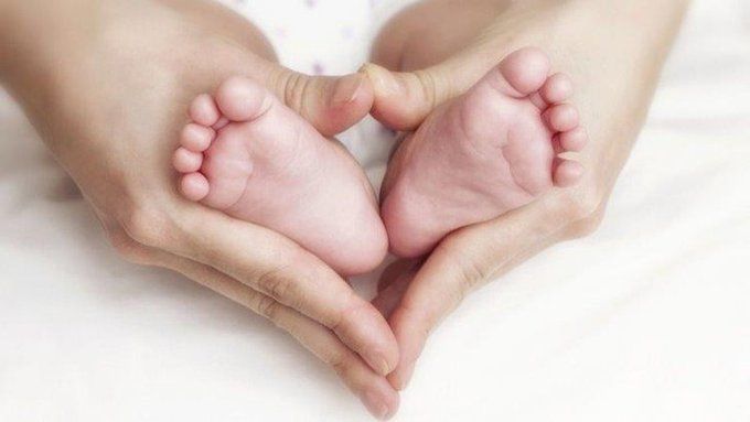 Baby feet inside mothers hands making a heart shape